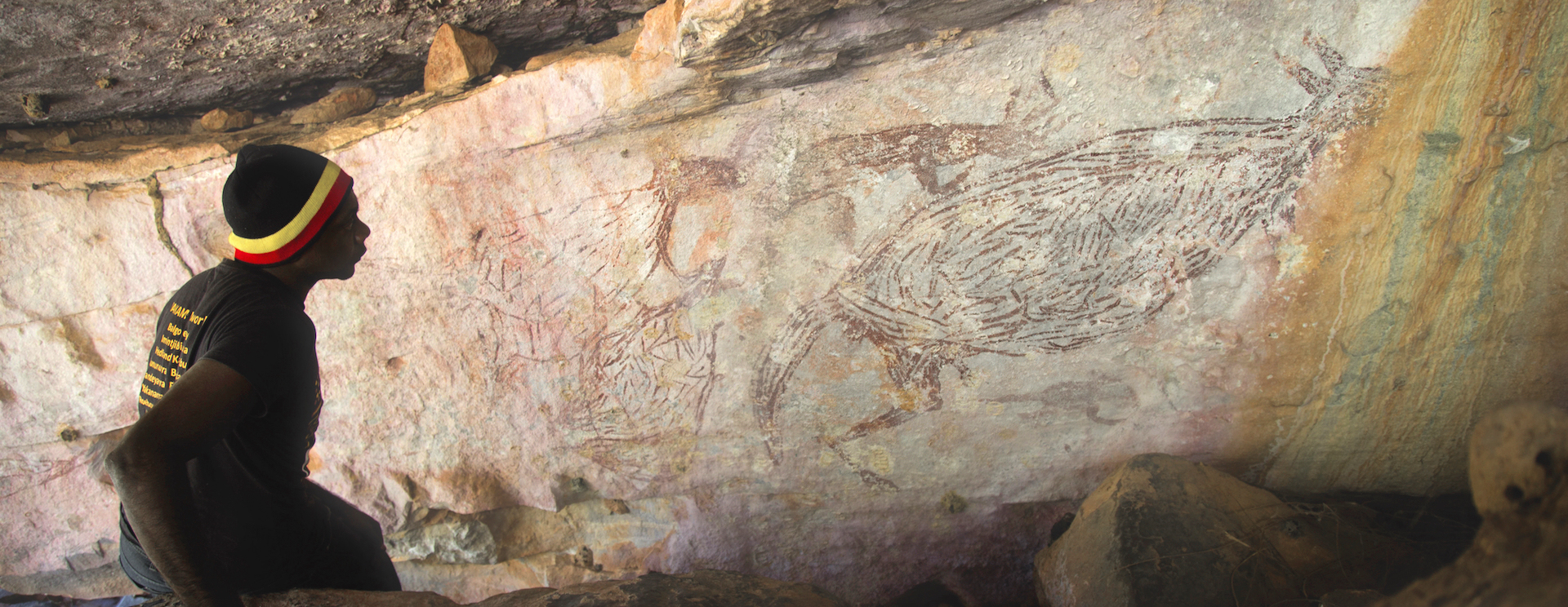 Traditional Owner Ian Waina inspecting a Naturalistic painting of a kangaroo. The inset is an illustration of the painting above it