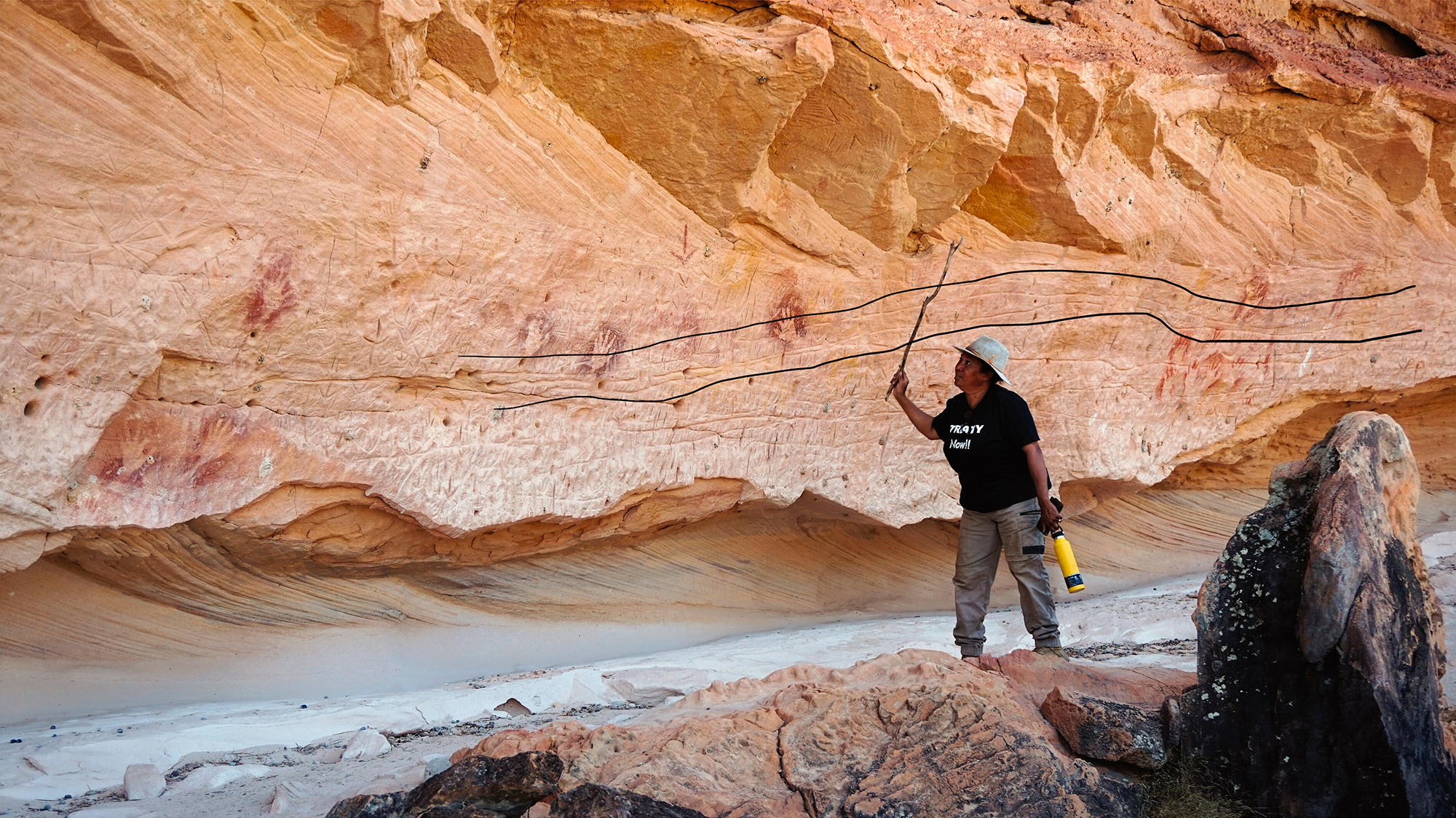 Suzanne Thompson in front of the engraved snake-like design, interpreted as a ‘Rainbow Serpent’ depiction (with black line showing its position). Thompson is explaining the significance of the rock art